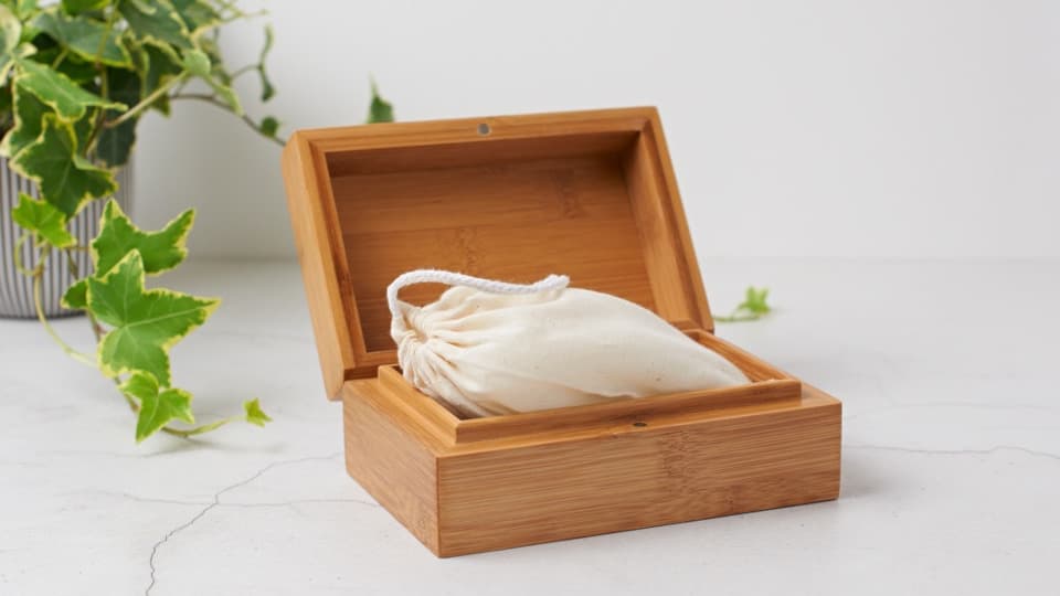 A light-coloured simple bamboo casket with rounded edges around the top. The casket opens from about two-thirds of the way up to reveal ashes in a cotton bag within. The lid is kept closed by a pair of magnets in the lid and side