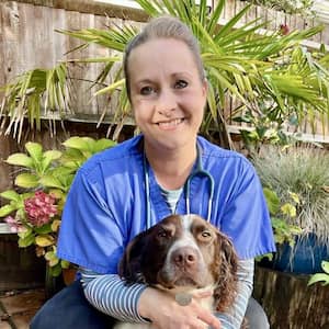 Profile picture of Sophie, a vet, in a garden with a hydrangea behind her, cuddling her Spaniel