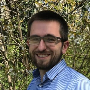 Profile picture of Ben, a vet. He is standing in front of green trees, facing slightly left and to camera with a short beard and glasses