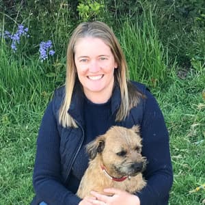 Profile picture of Rachel, a vet, crouching in a field and holding her Border Terrier